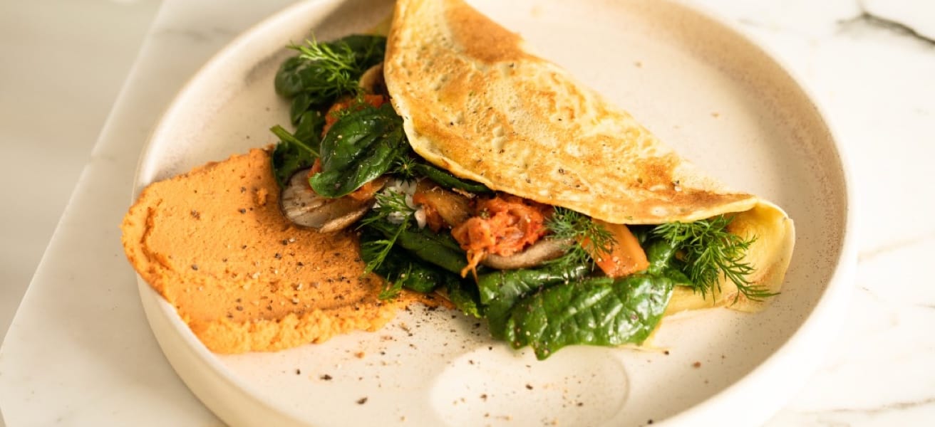 A folded golden omelette with fresh greens on a white plate
